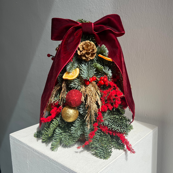 Decorative Christmas tree with a red bow on a white pedestal against a gray wall.