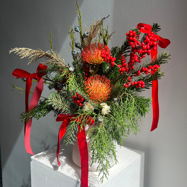 Decorative floral arrangement with red berries and ribbons on a white pedestal against a gray background