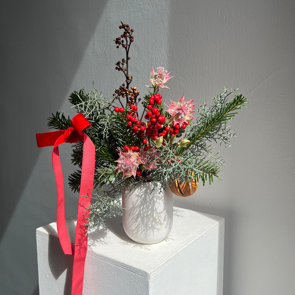 Decorative arrangement with flowers, berries, and a red ribbon on a white surface.