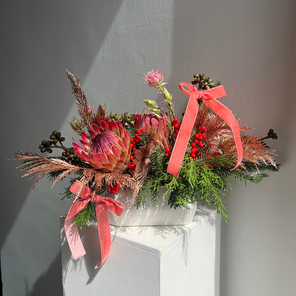 Decorative floral arrangement with pink ribbons on a white surface against a gray wall.