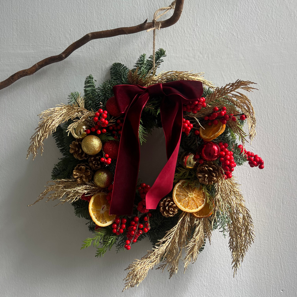 Decorative wreath with red ribbon, pinecones, and fruits on a plain background
