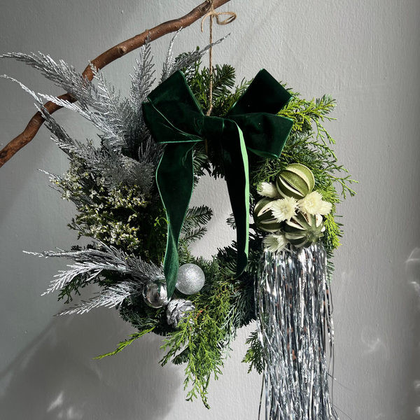 Decorative wreath with green bow, silver tinsel, and white berries on a plain background